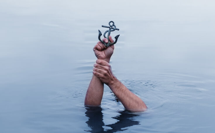Brazos de una persona saliendo del agua sujetando un ancla pequeña de metal